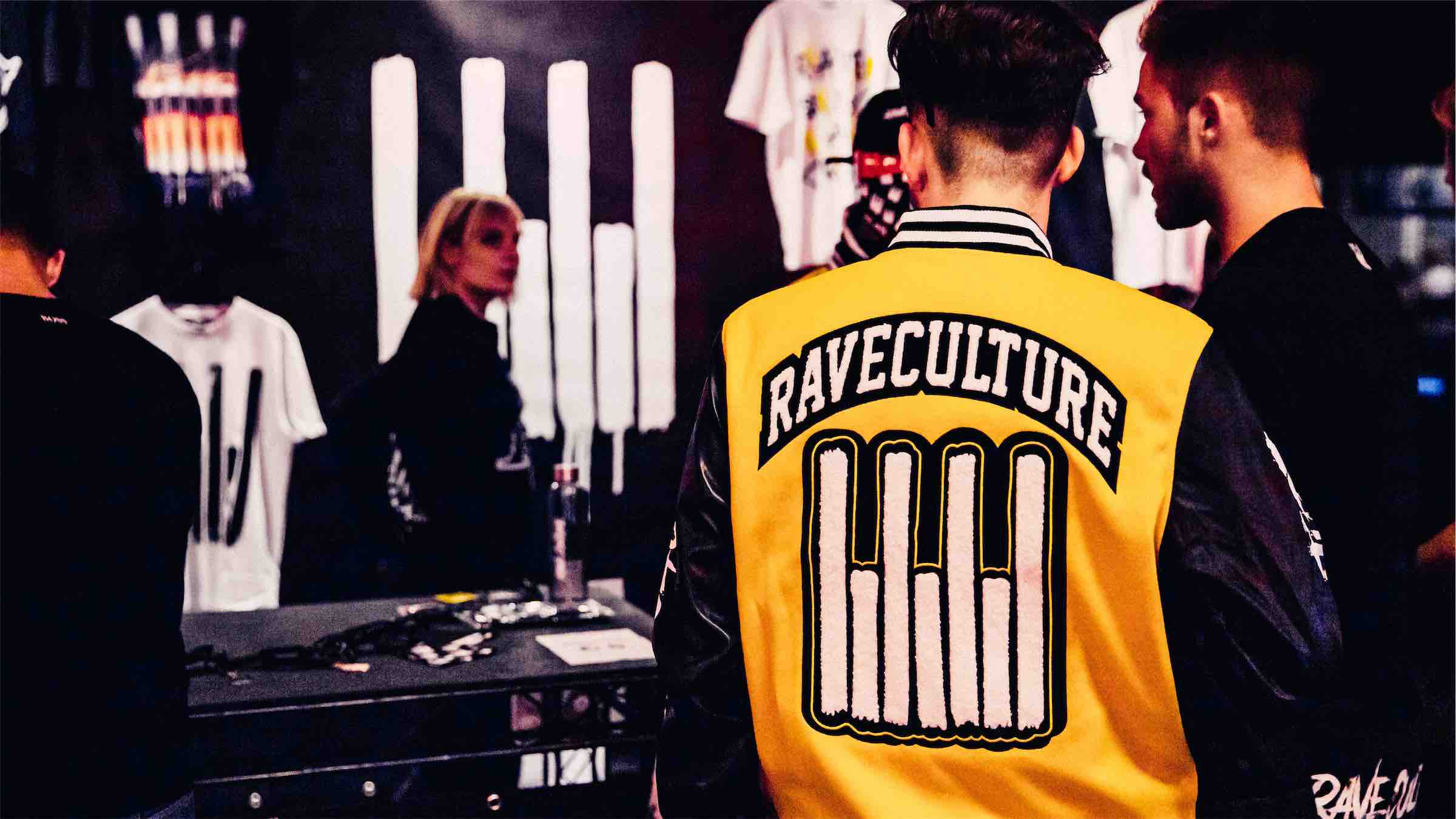 Raver wearing the Rave Culture Varsity Jacket at the Rave Culture ADE Pop-Up Shop. Visible in the back are the Metal Band T-Shirt, Emblem T-Shirt White and Rave Is Not A Crime Lightning T-Shirt.